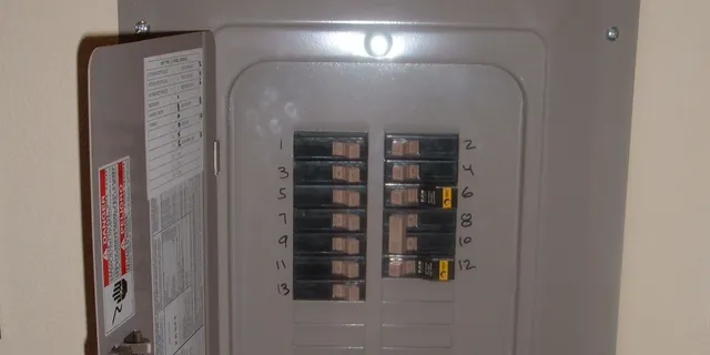 A home breaker panel with its door open and numbered breakers inside