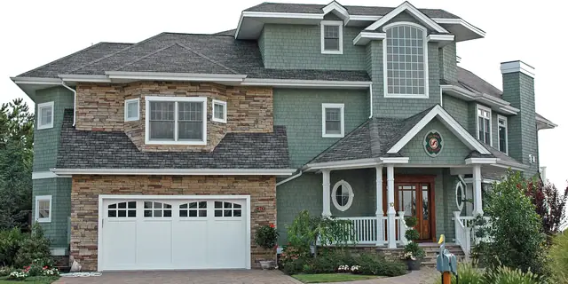 A big two-story house with a gray shingle roof, a green lawn and a front porch