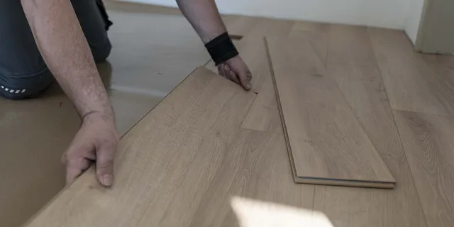 Hands fitting a new wood-look laminate floor board into place