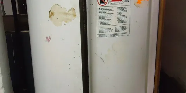 An old, worn tank water heater with peeling paint and warning labels